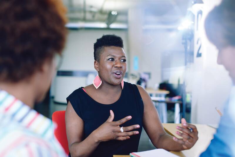 A woman speaking to two other people sat around a table.
