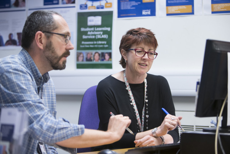 Two members of staff sat reading from a computer screen.