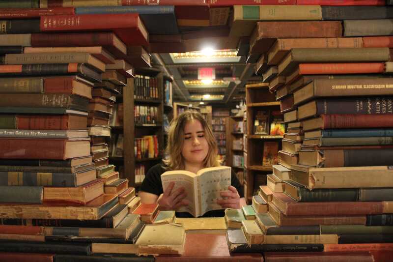 Student reading a book in a library framed by a circle of books.